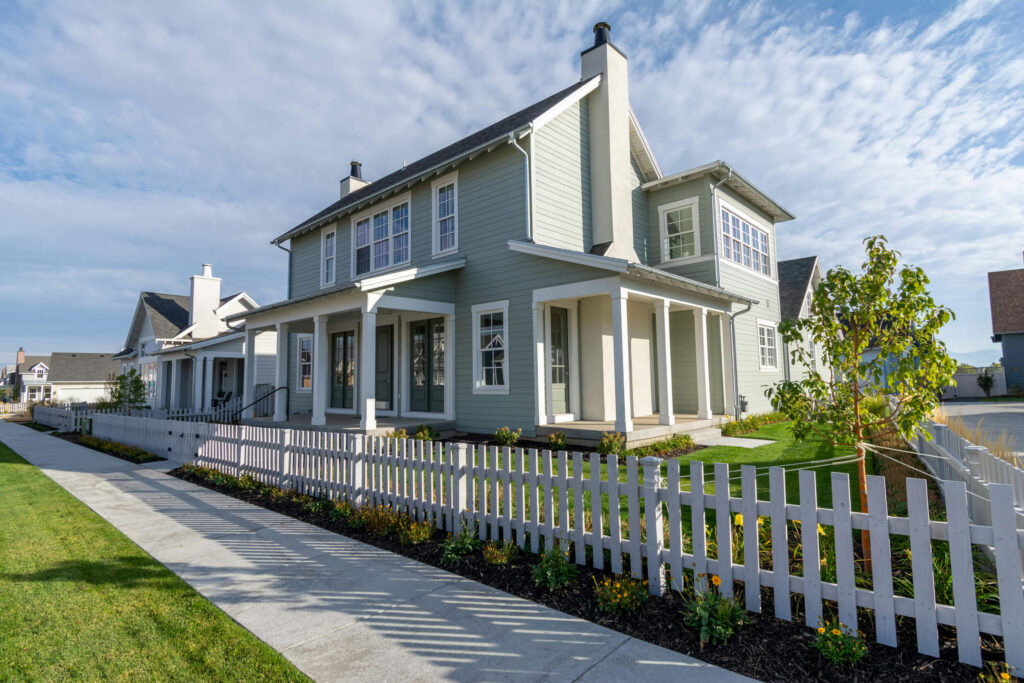 Image of modern two-story house with white picket fence, green lawn and blue sky